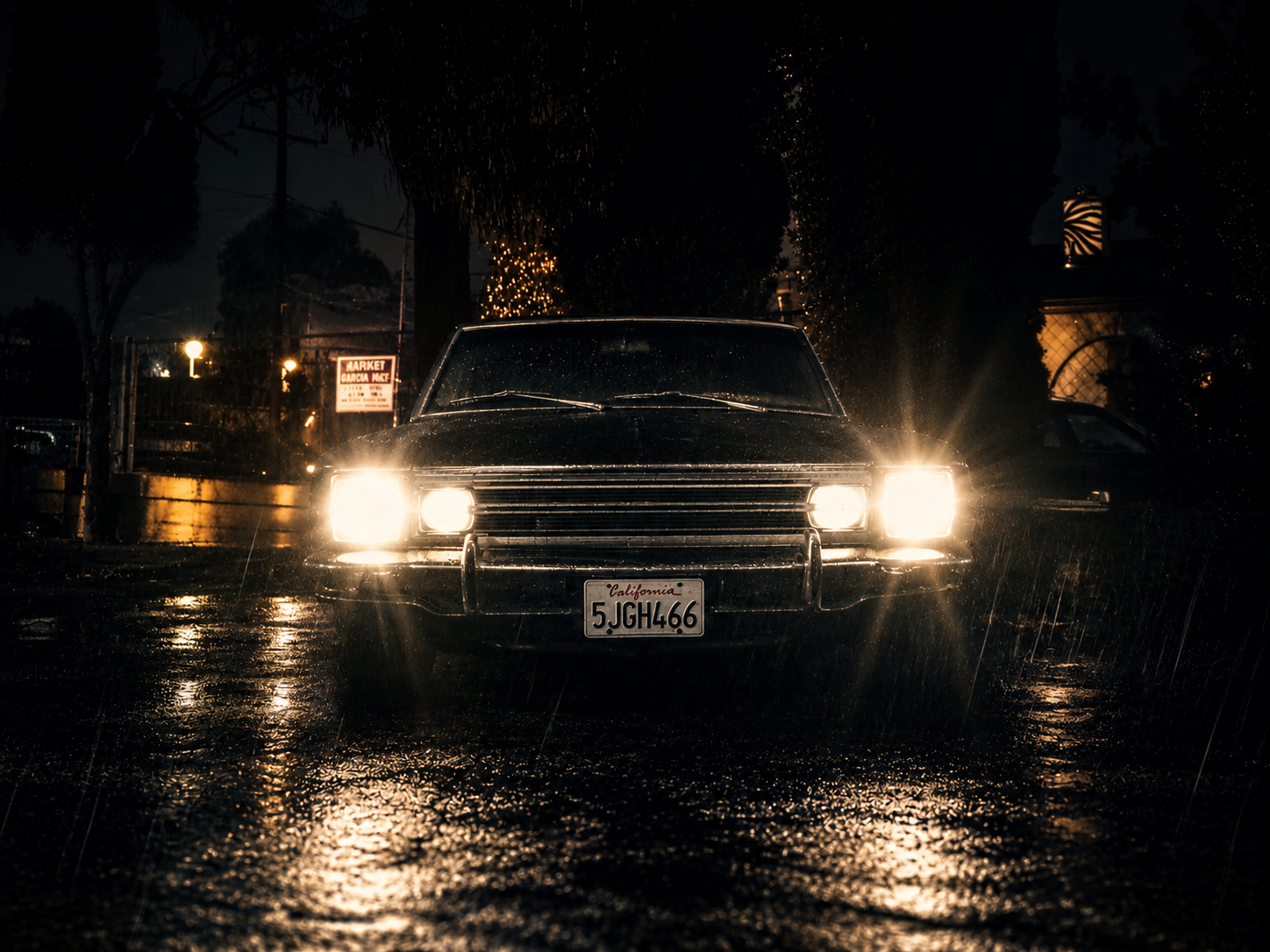 Classic black car with bright headlights on wet ground at night, raindrops visible, dark background with trees and streetlights.